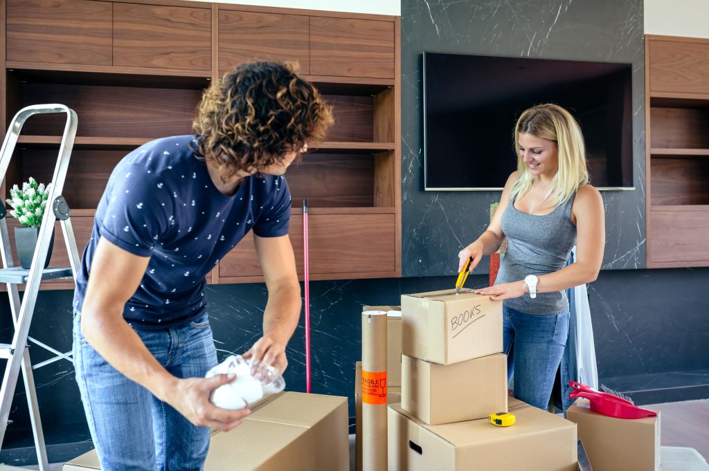 Couple packing cardboard boxes with household items for moving using efficient storage solutions.